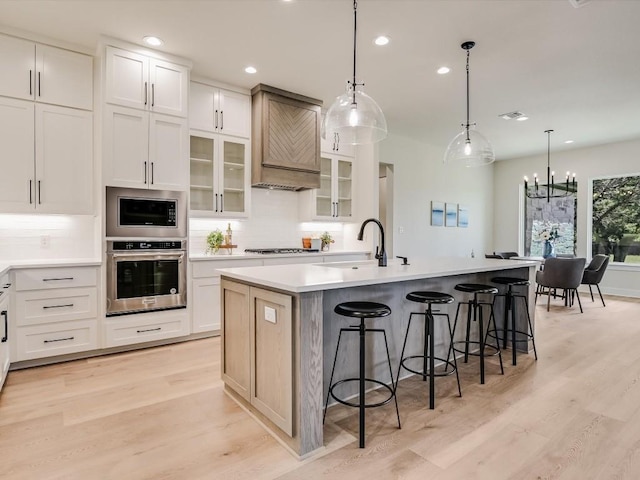 kitchen featuring sink, premium range hood, an island with sink, white cabinets, and appliances with stainless steel finishes