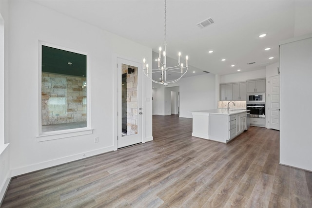 kitchen featuring a kitchen island with sink, sink, pendant lighting, hardwood / wood-style floors, and oven