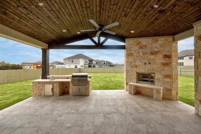 view of patio featuring ceiling fan, area for grilling, an outdoor stone fireplace, and exterior kitchen