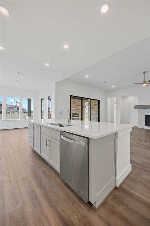 kitchen with white cabinets, a center island with sink, sink, stainless steel dishwasher, and wood-type flooring