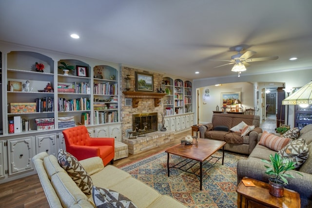 living room featuring wood-type flooring, ceiling fan, crown molding, and a large fireplace