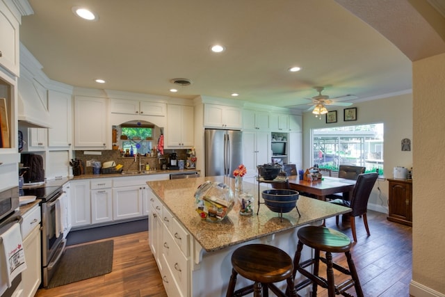 kitchen featuring appliances with stainless steel finishes, a kitchen island, ceiling fan, wood-type flooring, and white cabinetry