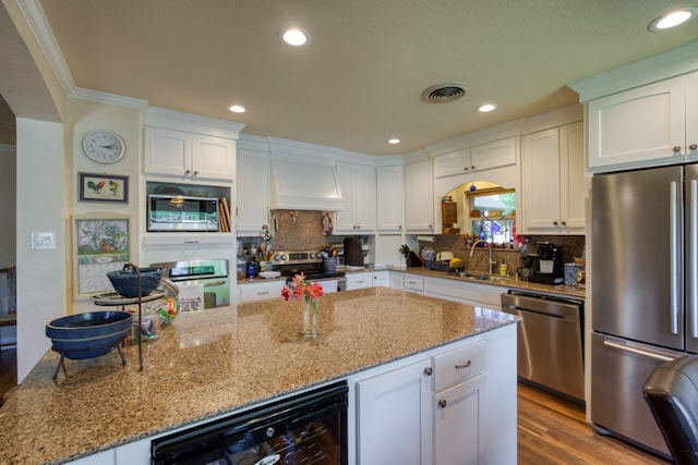 kitchen featuring premium range hood, backsplash, stainless steel appliances, white cabinets, and light wood-type flooring