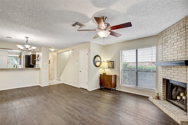 unfurnished living room with dark hardwood / wood-style flooring, a fireplace, a textured ceiling, and ceiling fan with notable chandelier