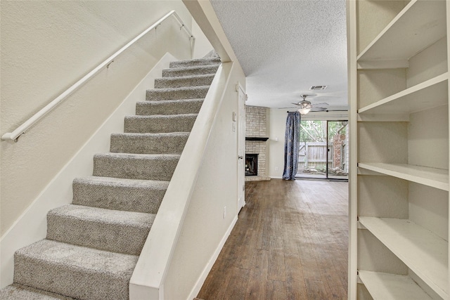 stairs featuring ceiling fan, brick wall, hardwood / wood-style floors, a fireplace, and a textured ceiling