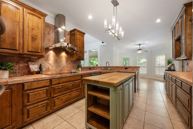 kitchen with light tile floors, wall chimney range hood, backsplash, ceiling fan with notable chandelier, and decorative light fixtures