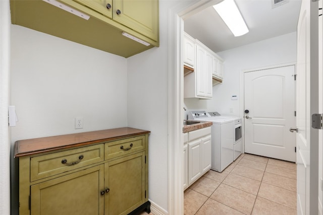 laundry room with cabinets, washing machine and dryer, and light tile floors