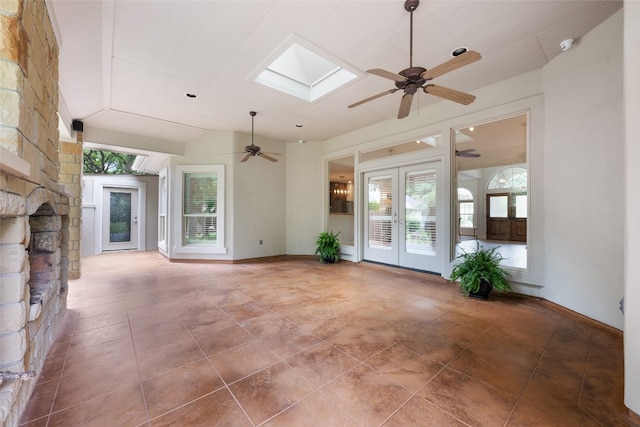 unfurnished living room with french doors, a stone fireplace, ceiling fan, tile flooring, and a skylight