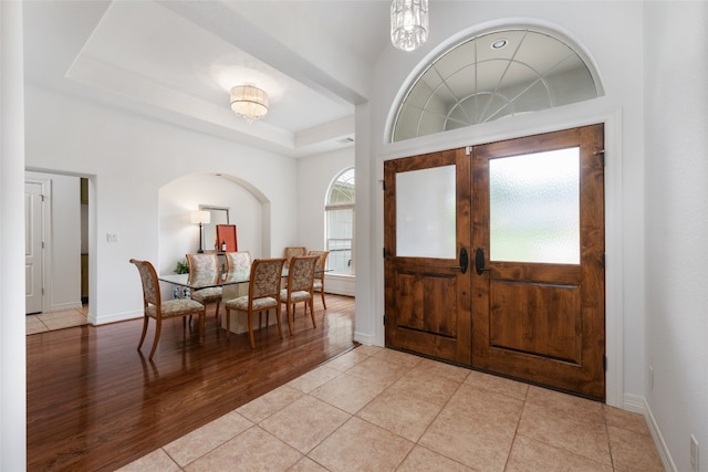 entrance foyer featuring french doors, light hardwood / wood-style floors, a chandelier, and a tray ceiling