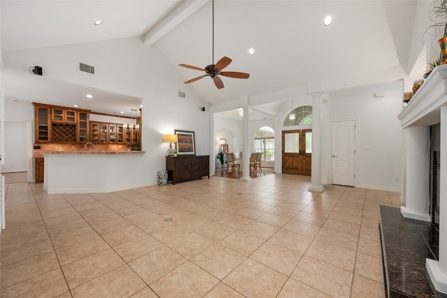 unfurnished living room featuring high vaulted ceiling, beamed ceiling, decorative columns, light tile floors, and ceiling fan