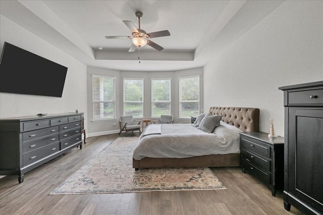 bedroom featuring light wood finished floors, ceiling fan, a tray ceiling, and baseboards