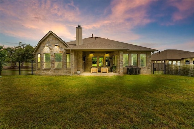 rear view of property with stone siding, a lawn, and a fenced backyard