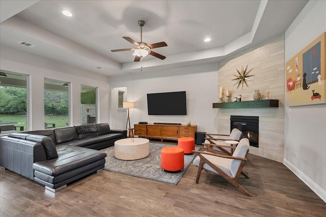 living room with wood finished floors, a tiled fireplace, a raised ceiling, and visible vents