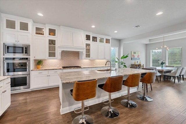 kitchen with glass insert cabinets, appliances with stainless steel finishes, and an island with sink