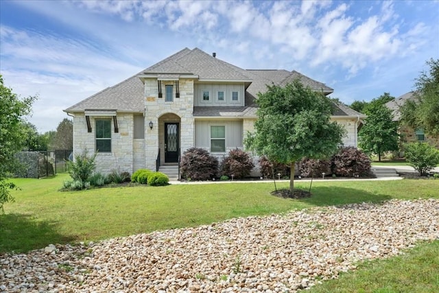 view of front of property featuring stone siding, fence, a front lawn, and roof with shingles