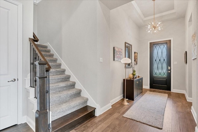 entrance foyer featuring a notable chandelier, wood finished floors, baseboards, stairs, and a raised ceiling