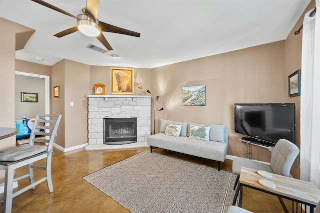 living room featuring a stone fireplace, ceiling fan, and concrete floors