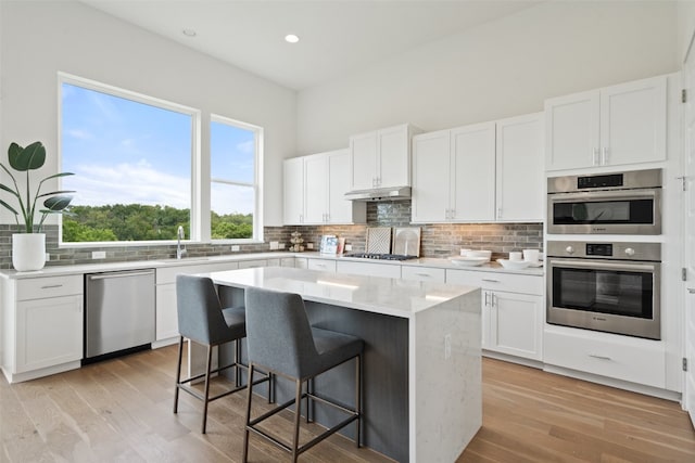 kitchen with a center island, light hardwood / wood-style flooring, backsplash, appliances with stainless steel finishes, and a breakfast bar area