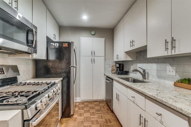 kitchen featuring stainless steel appliances, light parquet flooring, backsplash, sink, and white cabinetry