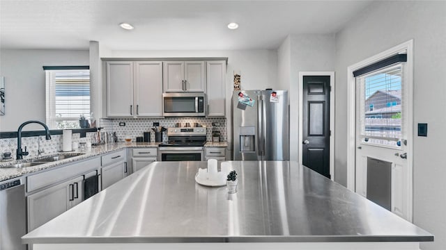 kitchen with gray cabinetry, backsplash, appliances with stainless steel finishes, sink, and a kitchen island