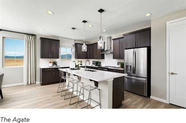 kitchen with stainless steel fridge with ice dispenser, light hardwood / wood-style flooring, wall chimney exhaust hood, and an island with sink