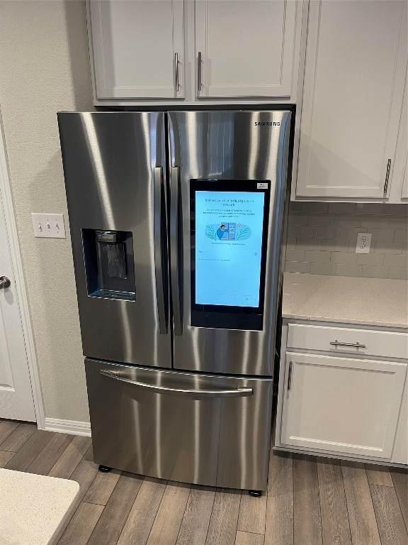 kitchen featuring white cabinetry, tasteful backsplash, wood-type flooring, and stainless steel fridge