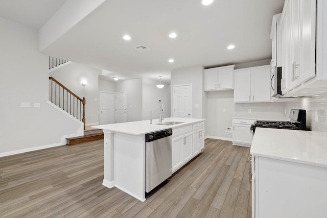 kitchen featuring light hardwood / wood-style flooring, appliances with stainless steel finishes, sink, tasteful backsplash, and an island with sink