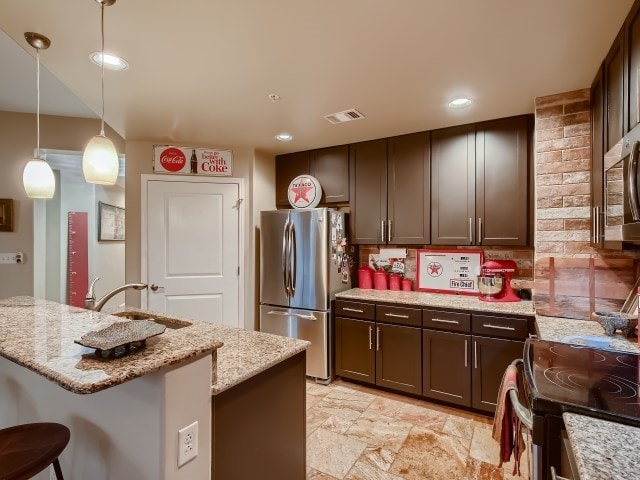 kitchen with decorative light fixtures, light stone counters, stainless steel fridge, and light tile flooring