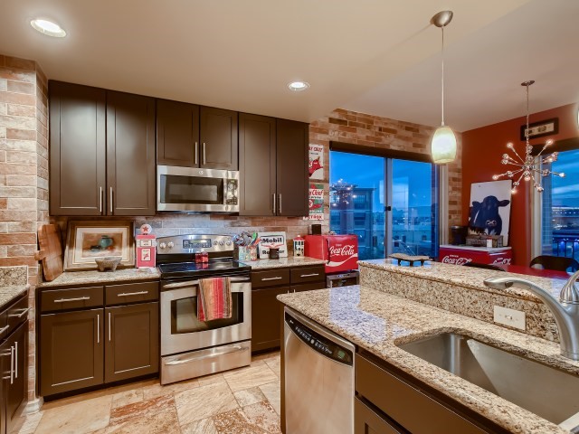 kitchen with decorative light fixtures, light tile flooring, appliances with stainless steel finishes, sink, and light stone counters