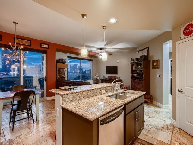 kitchen featuring light stone counters, pendant lighting, light tile flooring, a center island with sink, and stainless steel dishwasher