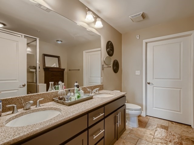 bathroom featuring toilet, tile flooring, and double sink vanity