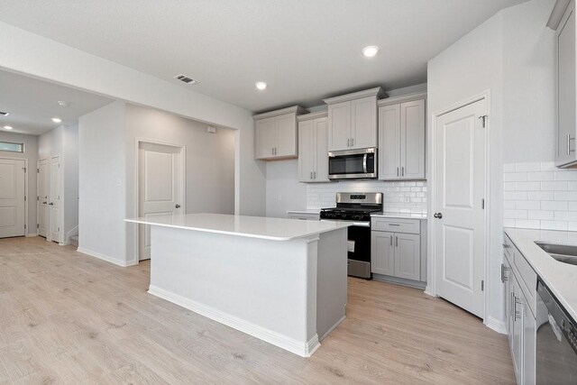 kitchen featuring light hardwood / wood-style floors, appliances with stainless steel finishes, tasteful backsplash, and a kitchen island