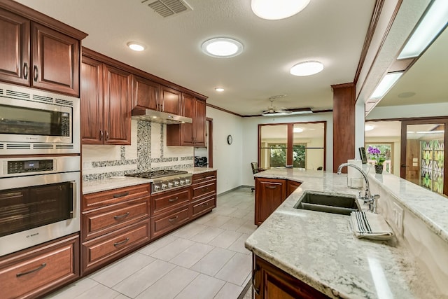 kitchen featuring appliances with stainless steel finishes, backsplash, sink, light stone counters, and ceiling fan