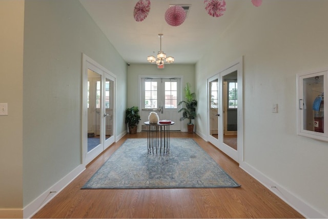 unfurnished dining area with an inviting chandelier, french doors, and wood-type flooring