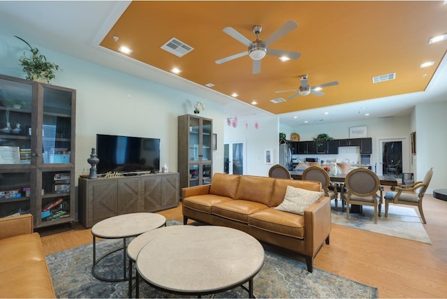 living room featuring ceiling fan, light wood-type flooring, and a tray ceiling