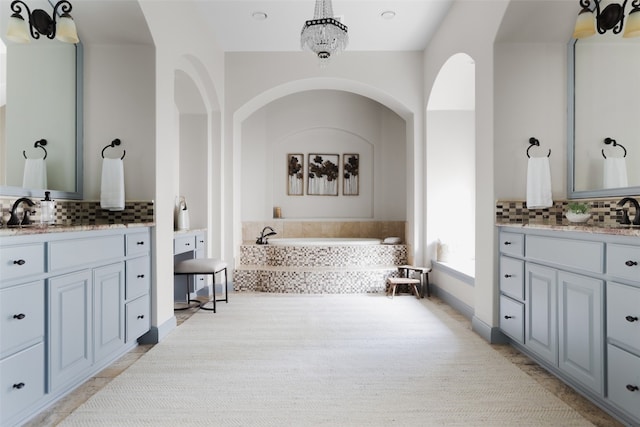 bathroom with a notable chandelier, a relaxing tiled tub, and vanity