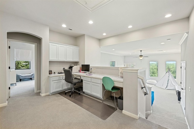 home office with built in desk, light colored carpet, and ceiling fan