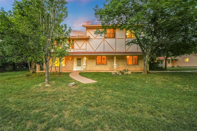 back of house at dusk with brick siding and a lawn