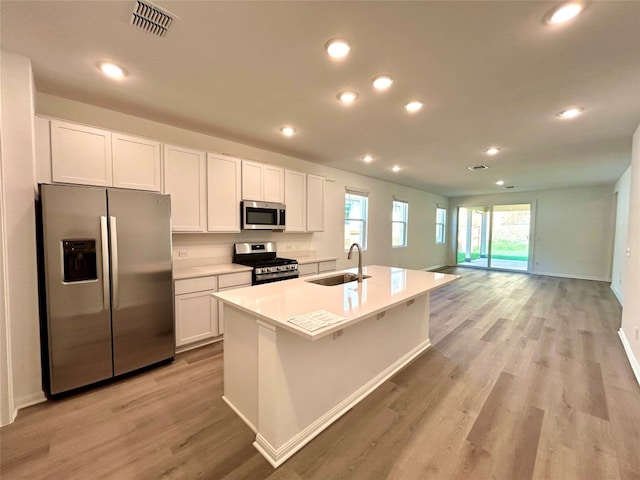 kitchen with appliances with stainless steel finishes, white cabinetry, sink, and an island with sink