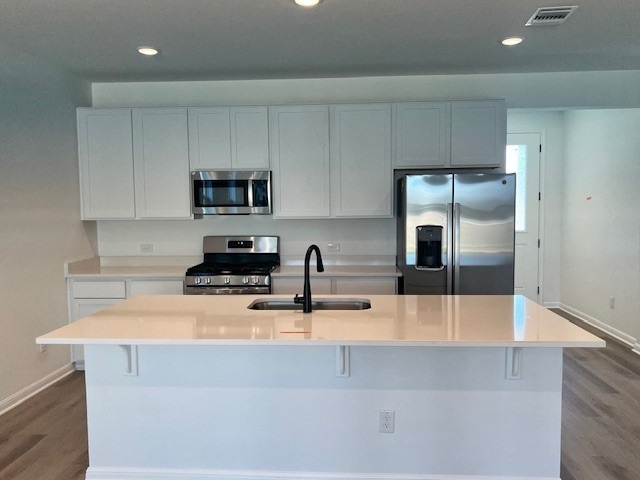 kitchen with a spacious island, white cabinetry, hardwood / wood-style flooring, sink, and stainless steel appliances