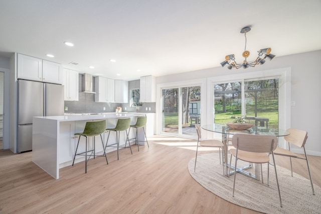 kitchen with tasteful backsplash, white cabinets, light wood-type flooring, wall chimney exhaust hood, and stainless steel fridge