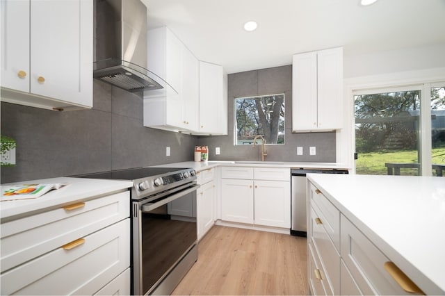 kitchen featuring a healthy amount of sunlight, appliances with stainless steel finishes, wall chimney exhaust hood, and white cabinetry