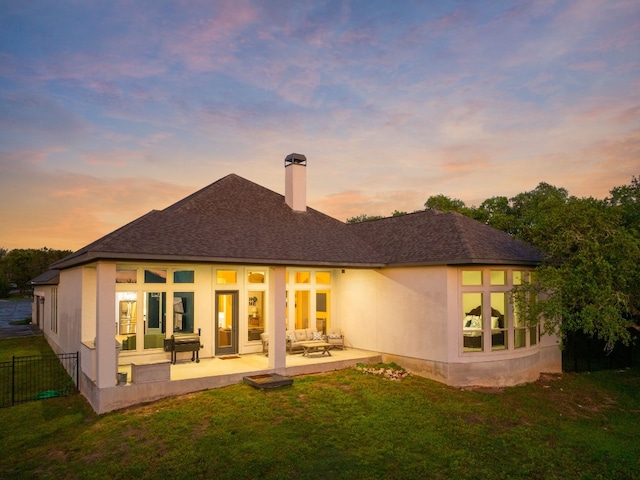 back house at dusk featuring a patio and a yard