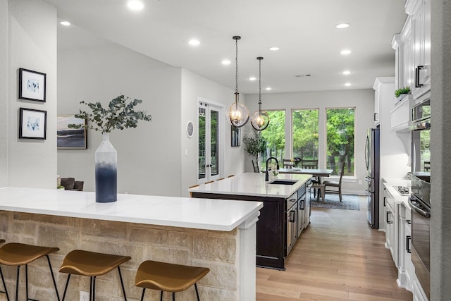 kitchen featuring white cabinetry, a kitchen island with sink, light hardwood / wood-style flooring, decorative light fixtures, and sink