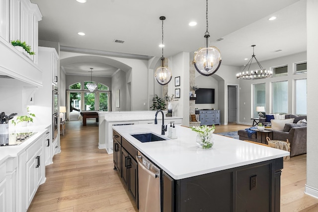 kitchen with a kitchen island with sink, light wood-type flooring, dishwasher, decorative light fixtures, and sink