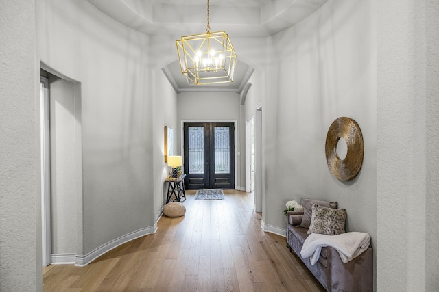 foyer featuring a raised ceiling, an inviting chandelier, hardwood / wood-style flooring, ornamental molding, and french doors