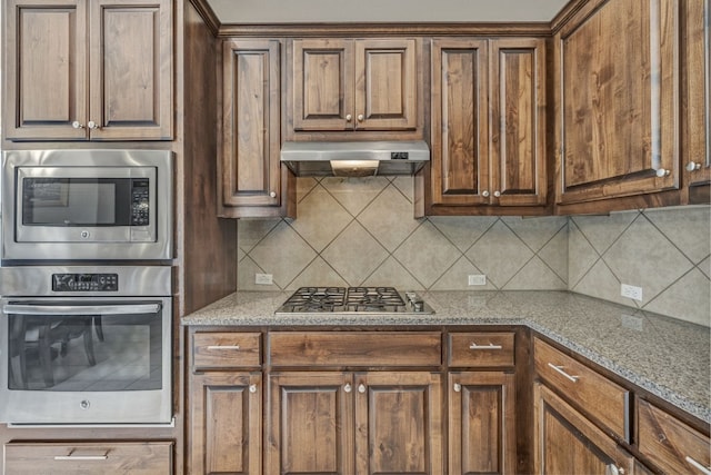 kitchen with backsplash, appliances with stainless steel finishes, wall chimney range hood, and light stone countertops