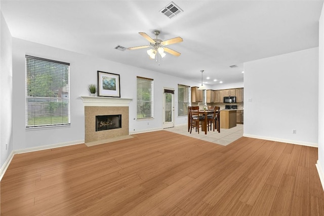 unfurnished living room with a tile fireplace, light hardwood / wood-style floors, and ceiling fan