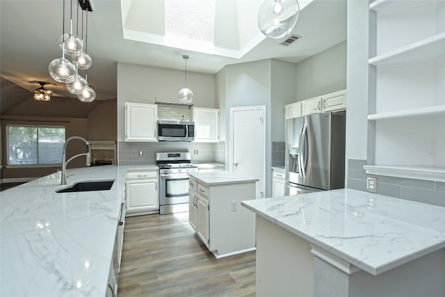 kitchen with stainless steel appliances, sink, light stone counters, a center island, and white cabinets