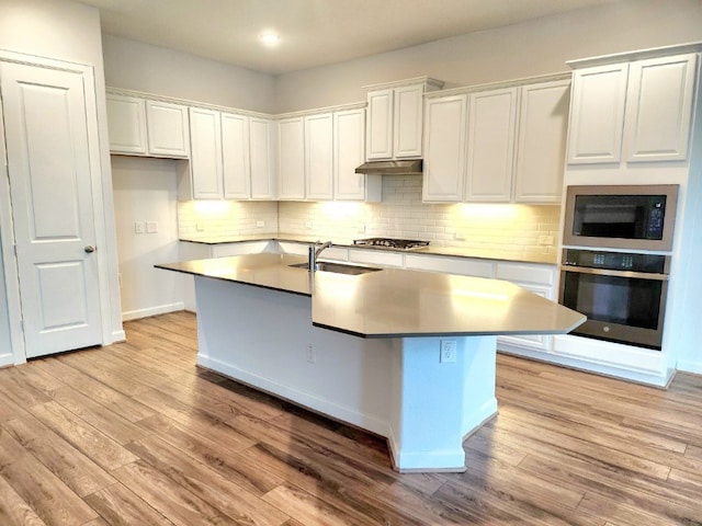 kitchen featuring appliances with stainless steel finishes, light hardwood / wood-style floors, tasteful backsplash, an island with sink, and white cabinets